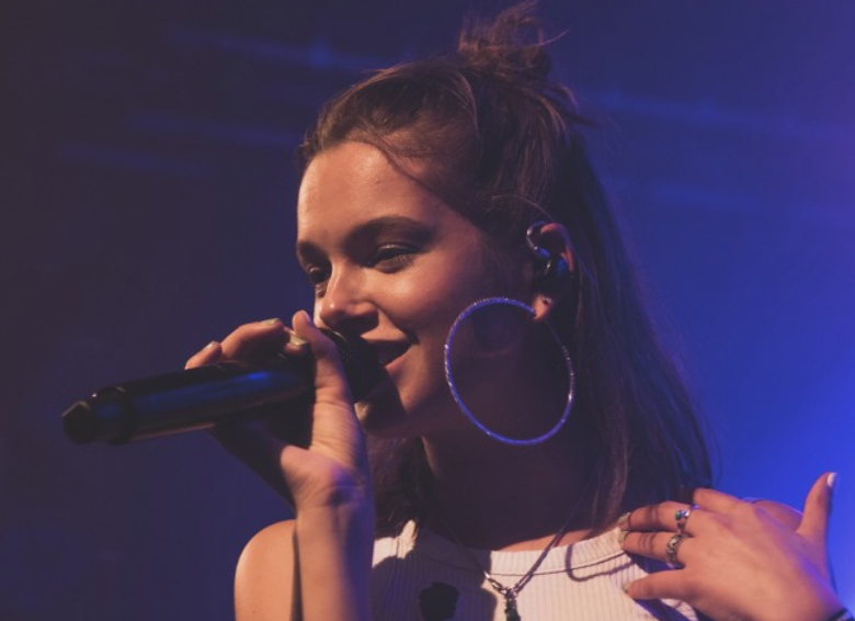 Head shot of Dayyani performing at an arena, holding a microphone and wearing hooped earrings.